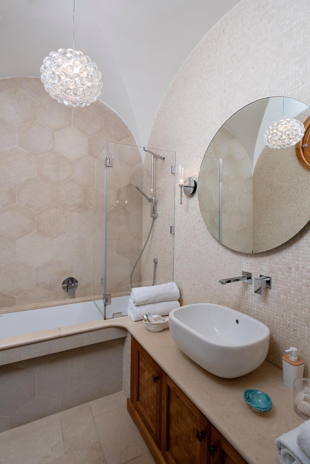 Il bagno con soffitto a volta in travertino esagonale, lampadario in cristallo e vasca in nicchia