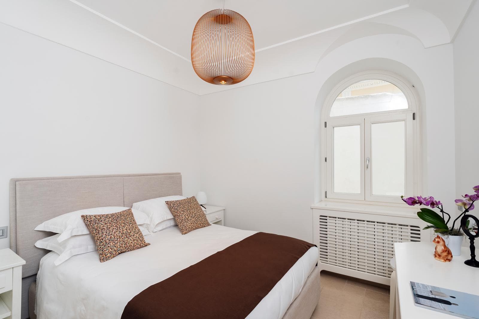 La camera con pendant in rame Foscarini, testiera in lino, soffitto a volta e finestra ad arco