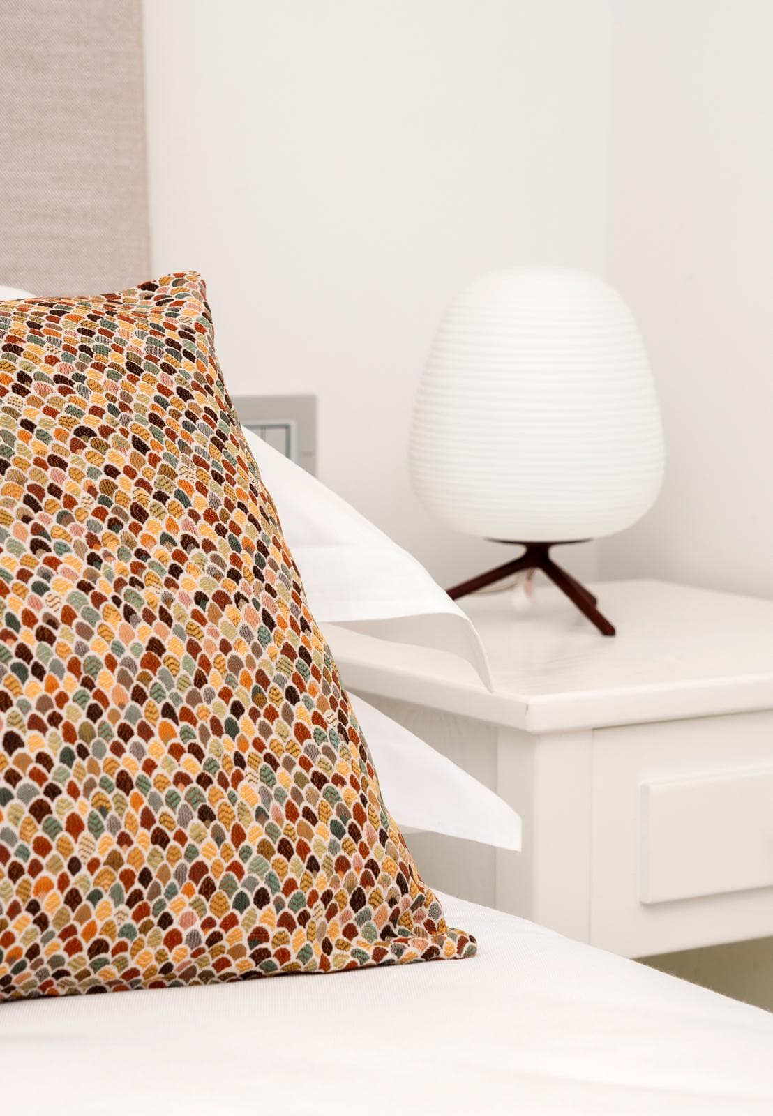 Dettaglio: cuscino a mosaico in toni rame e lampada in vetro Foscarini sul comodino